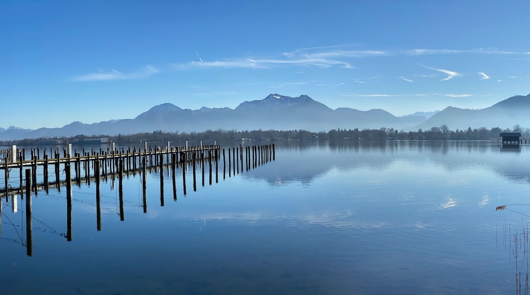 A calm lake with a wooden dock extending into the water, surrounded by mountains and sparse trees.