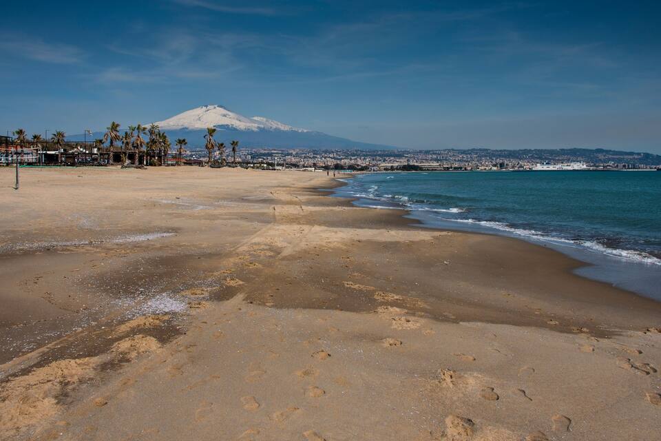 Una playa con huellas, una montaña y una ciudad al fondo.