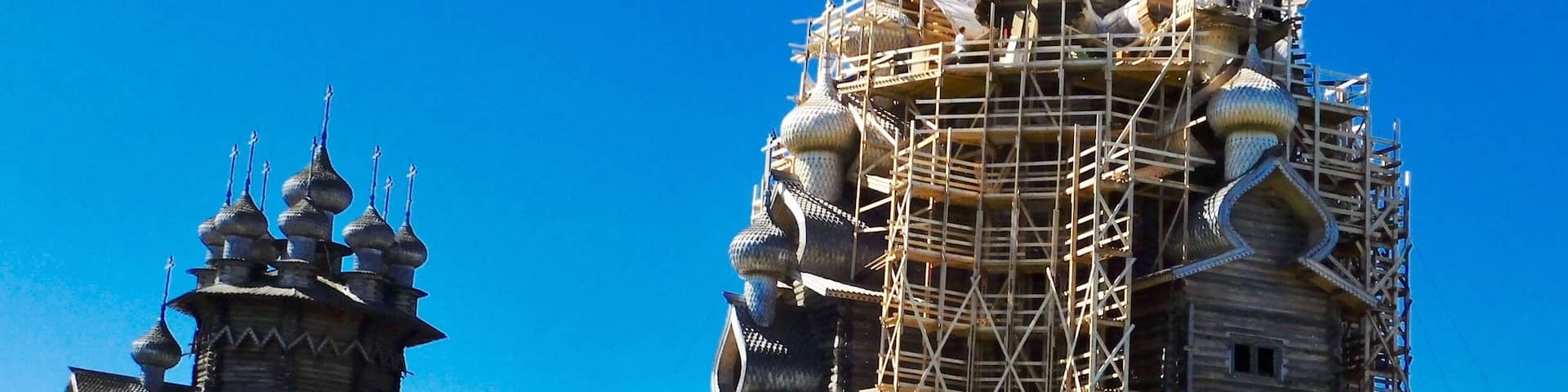 A historic wooden church with ornate domes and a large building under construction with scaffolding.