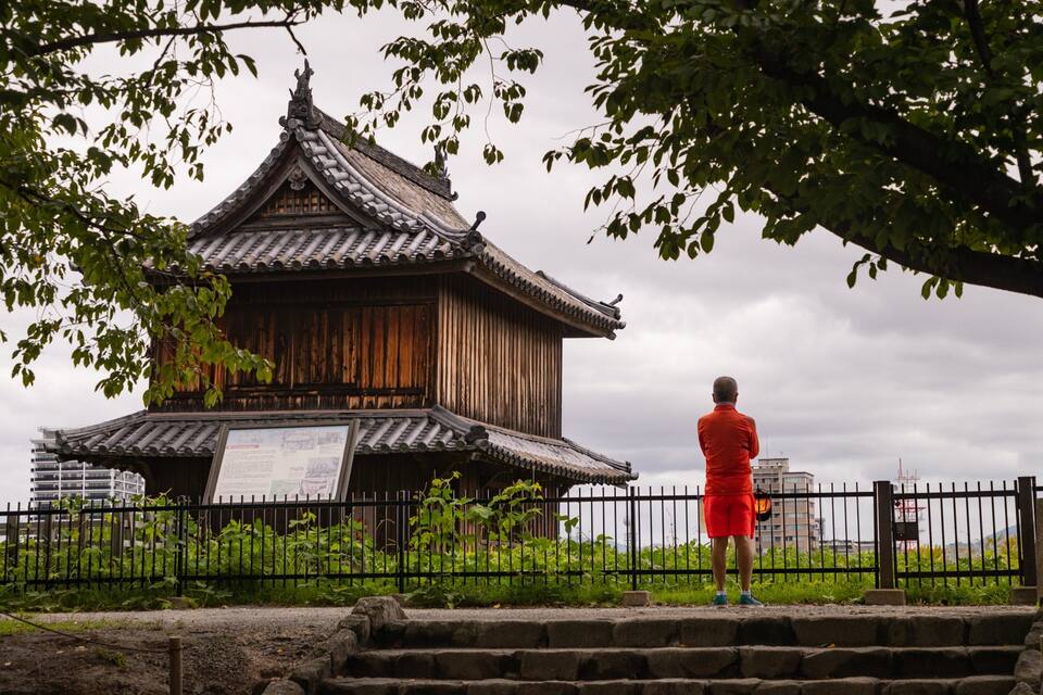 En traditionel træpagode med et tag af fliser, omgivet af et sort metalhegn og grønt.