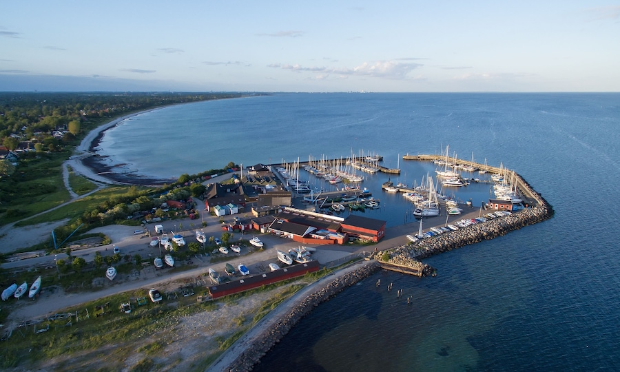 An aerial view of a coastal marina with boats docked, a pier, and surrounding residential areas.