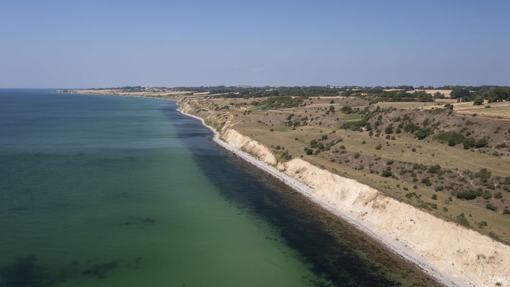 Aerial view of the striking contrast between the turquoise sea and the rugged coastline, a symphony of natural beauty unfolds, Aeroskobing, Southern Denmark, Denmark.