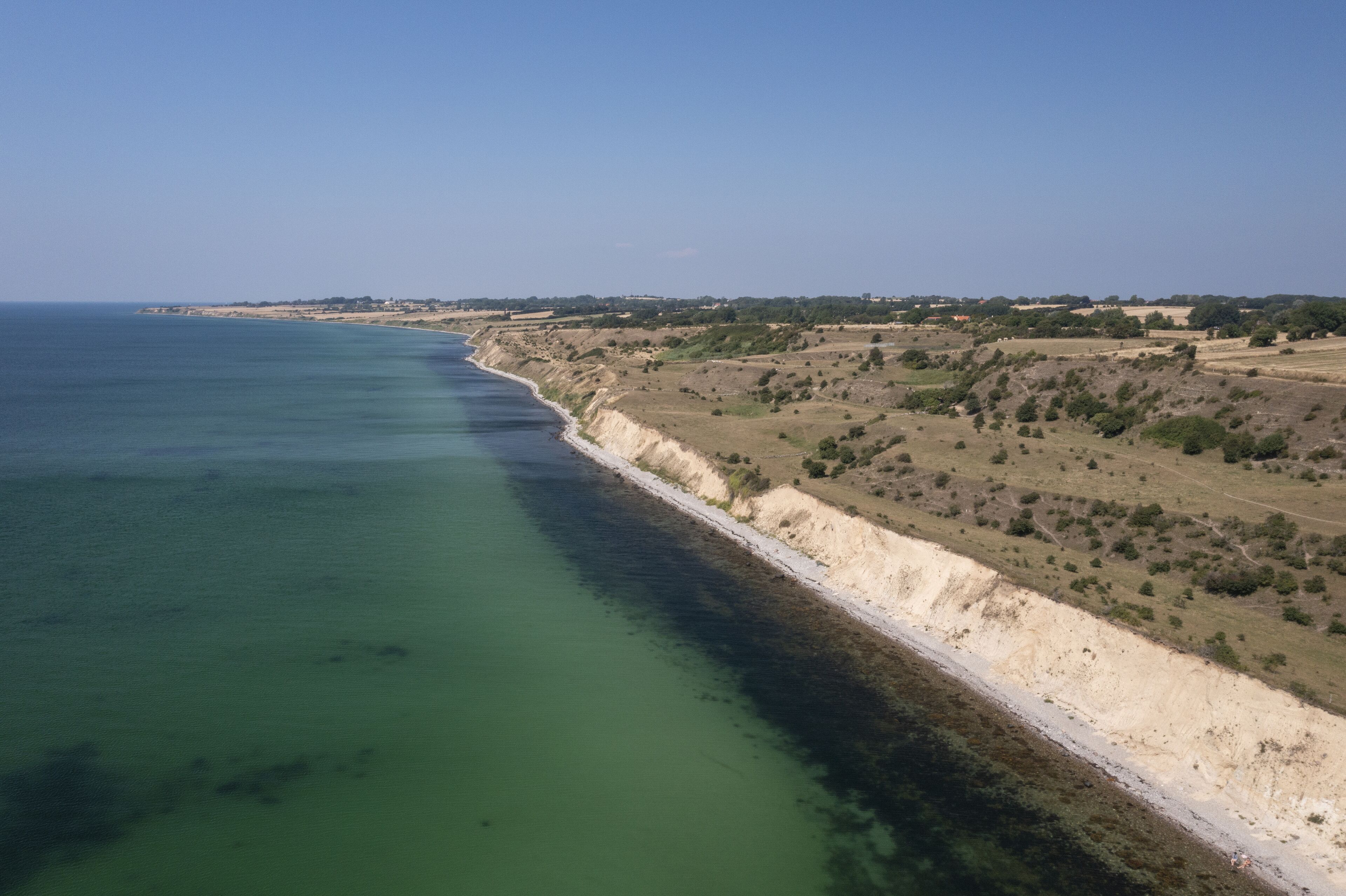 A coastal landscape with a clear coastline, sandy beaches, and sparse vegetation.