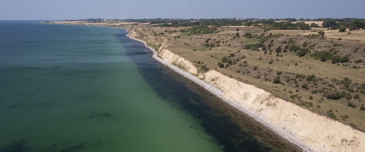 A coastal landscape with a clear coastline, sandy beaches, and sparse vegetation.