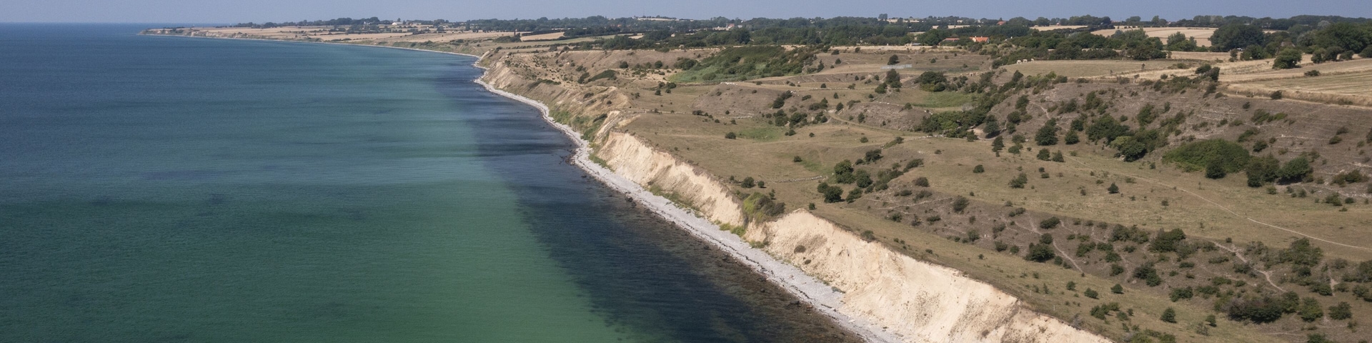 A coastal landscape with a clear coastline, sandy beaches, and sparse vegetation.