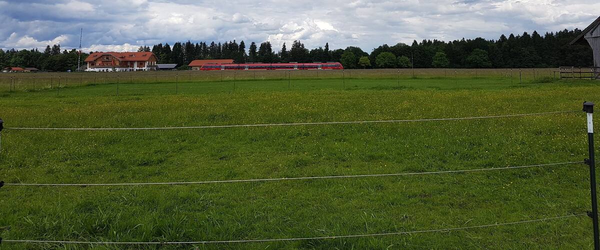 A rural landscape with a green field, a red building, and a cloudy sky.