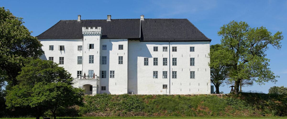 A large white building with a black roof, surrounded by trees and a grassy field.