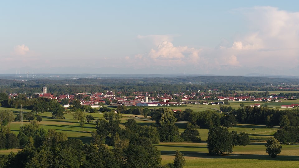 A town with red-roofed buildings, green fields, and distant mountains.