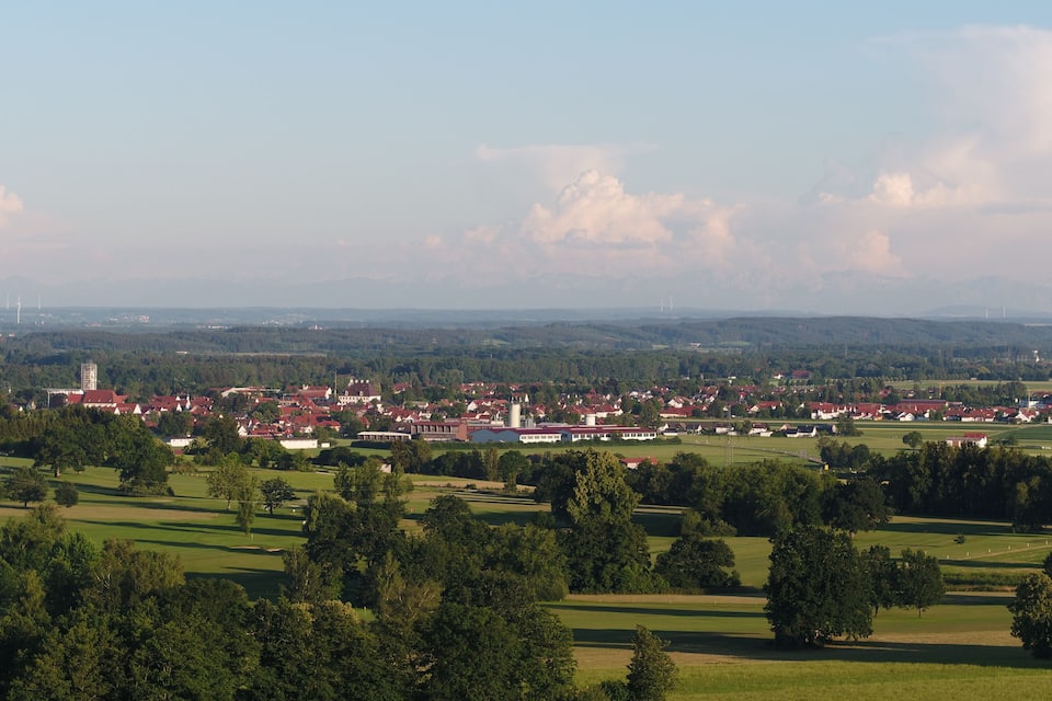 A town with red-roofed buildings, green fields, and distant mountains.