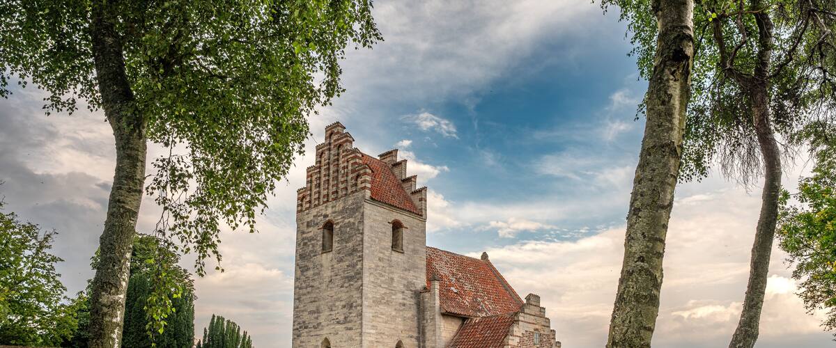A historic stone tower with a red-tiled roof, surrounded by a stone wall and lush green grass.