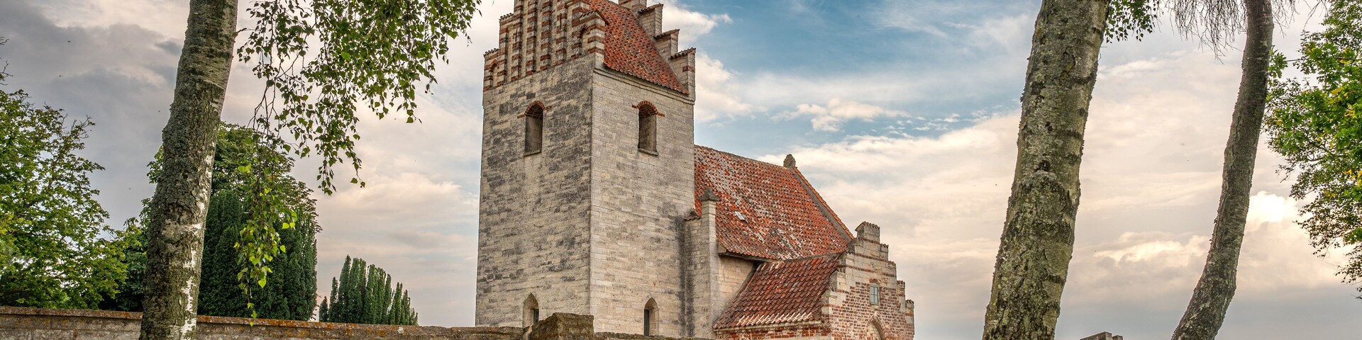 A historic stone tower with a red-tiled roof, surrounded by a stone wall and lush green grass.