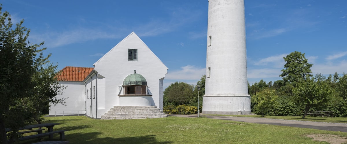 A white lighthouse with a green dome, a white building with a red roof, and a clear blue sky.