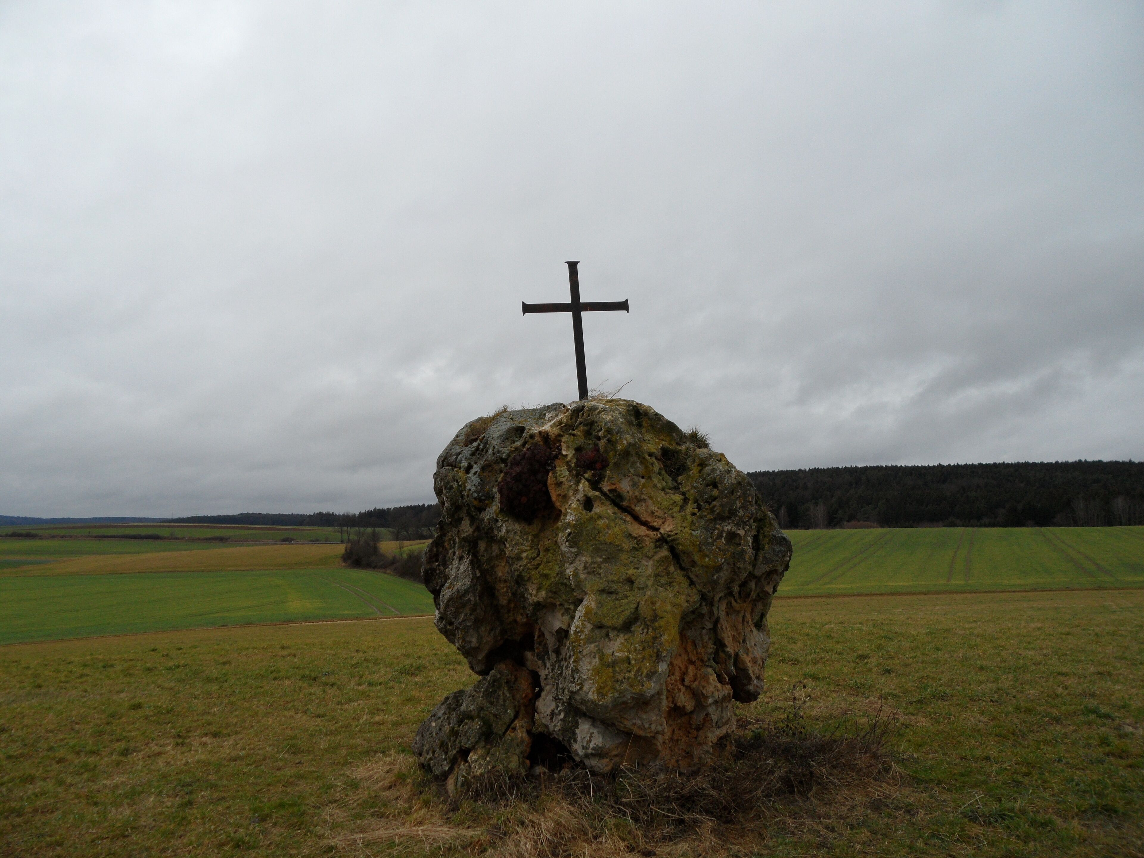 A cross on a rock in a grassy field.