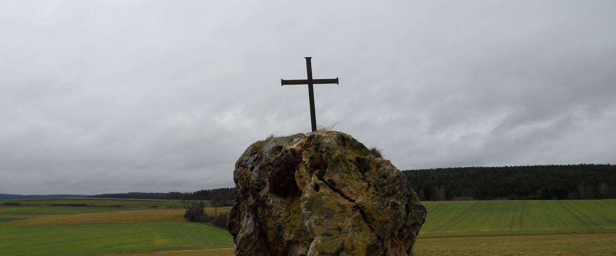 A cross on a rock in a grassy field.
