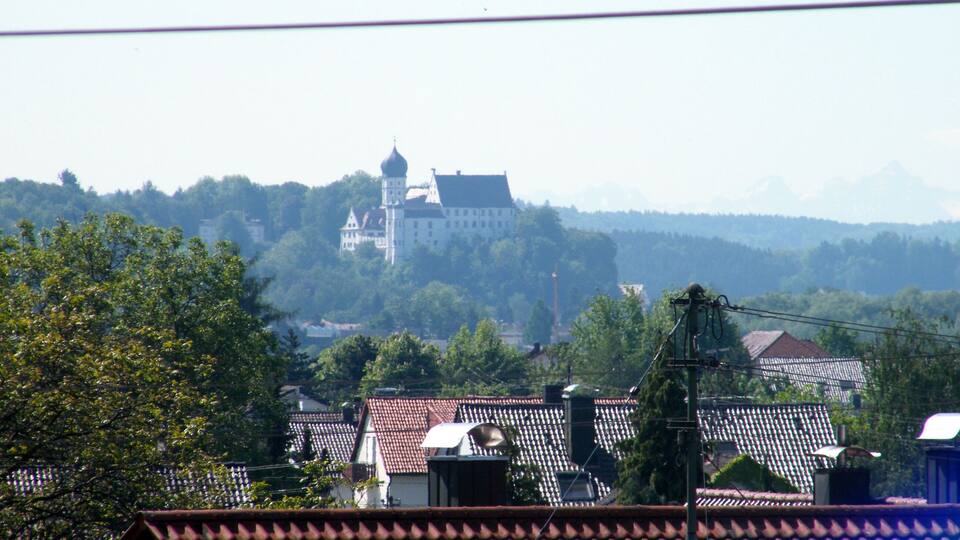 A castle on a hill with a red-tiled roof village in the foreground.