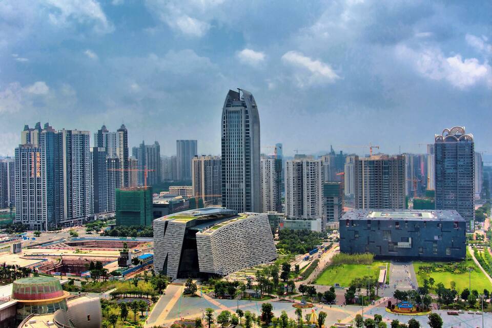 A cityscape with modern high-rise buildings, a distinctive curved building, and a large open plaza.
