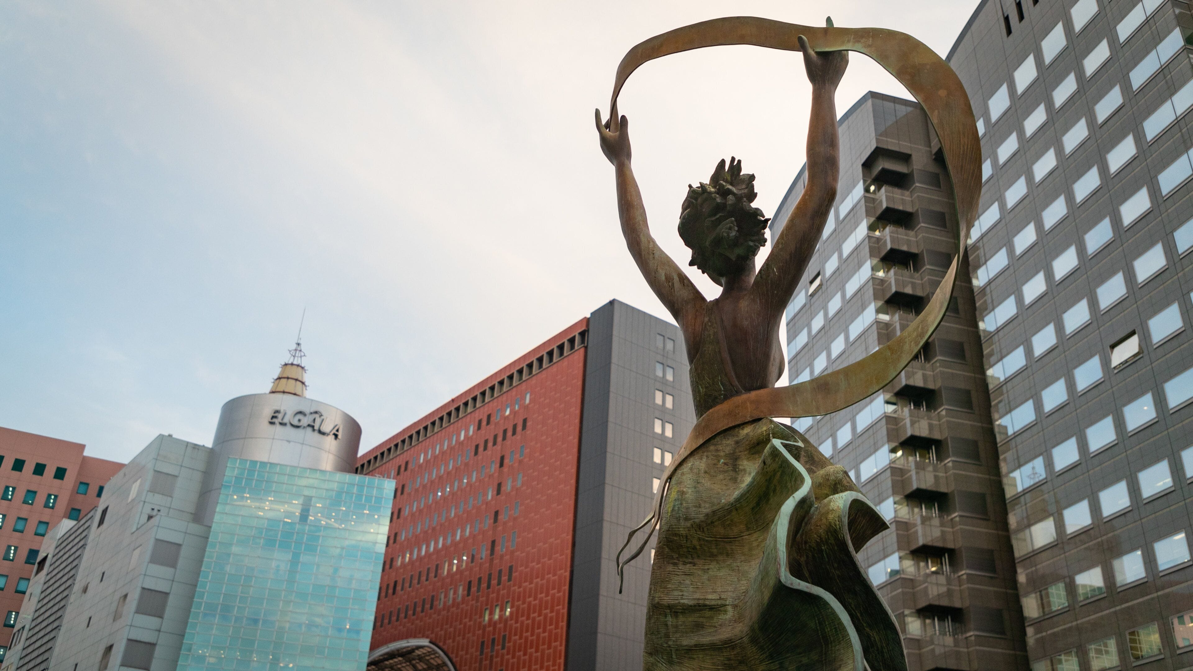 A sculpture of a person holding a ring, with modern buildings in the background.