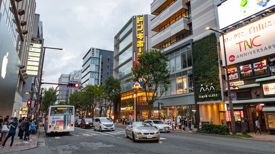 Eine belebte Stadtstraße mit modernen Gebäuden, darunter ein auffälliges Schild von TNC, sowie verschiedenen Geschäften und Restaurants.