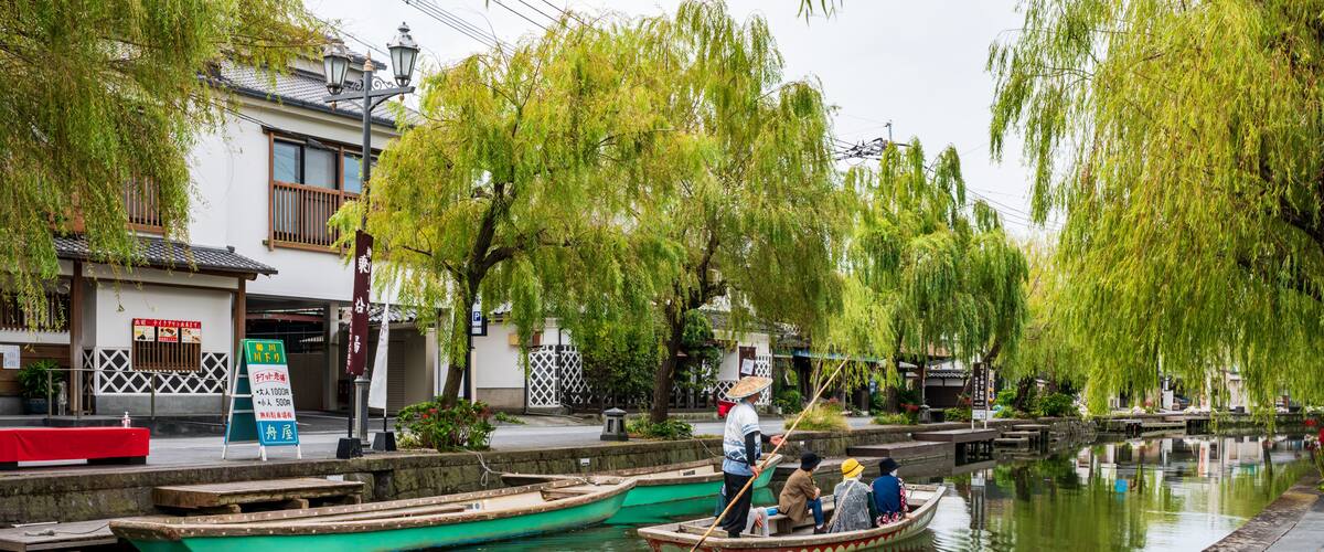 A traditional canal scene with boats, willow trees, and a building with signage.