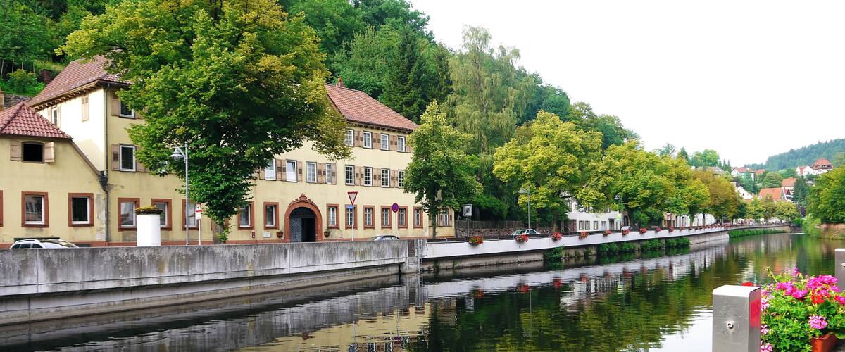 A calm river with a bridge, buildings, and trees along the banks.