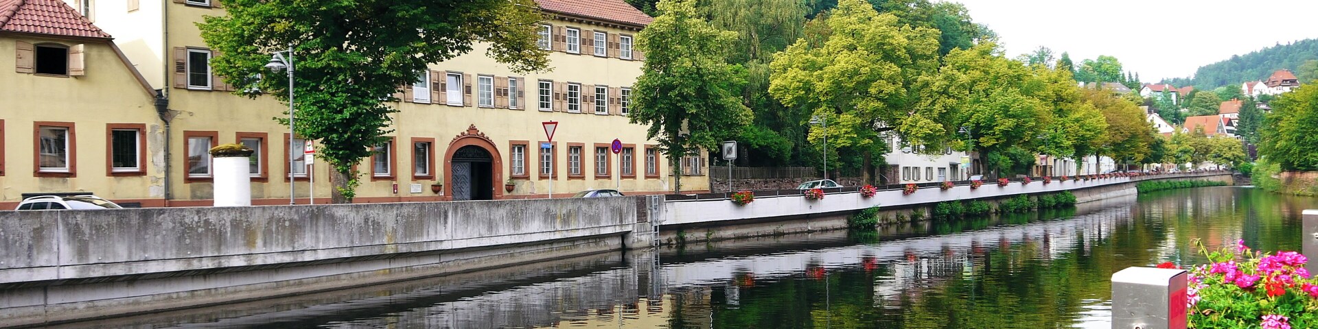 A calm river with a bridge, buildings, and trees along the banks.