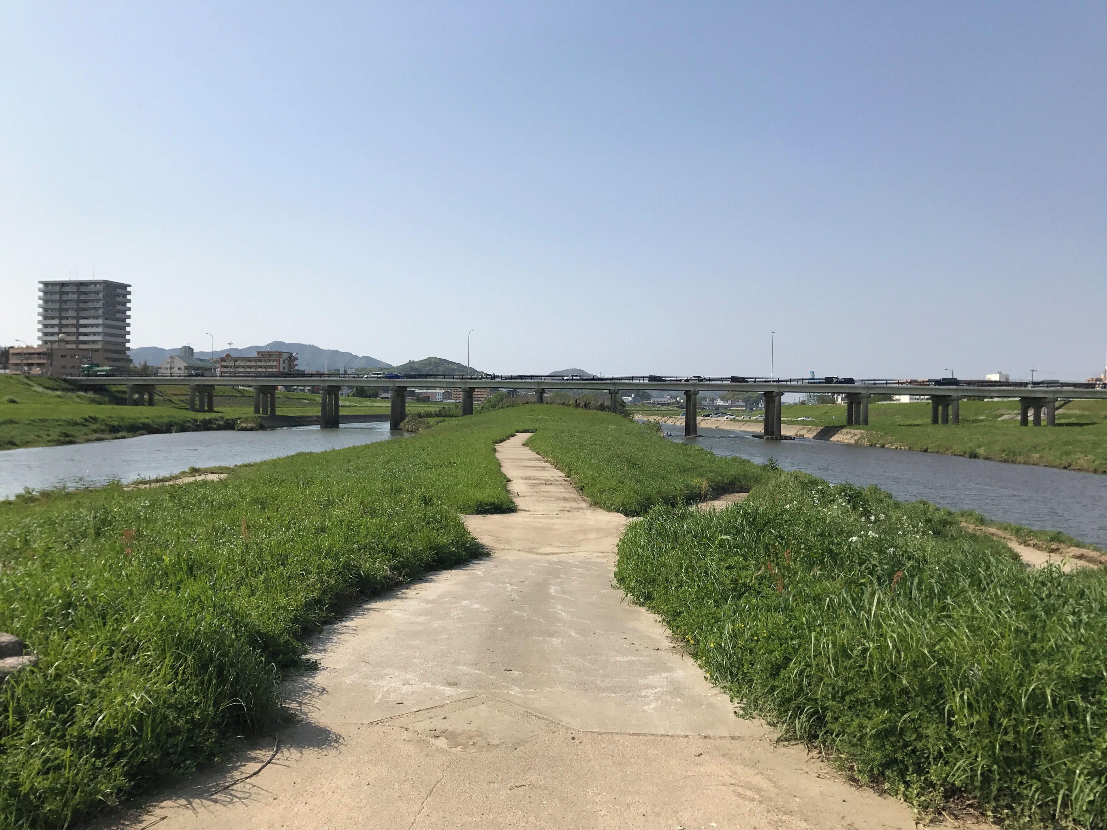 Un sendero de concreto bordeado por césped verde que conduce a un puente sobre un río.