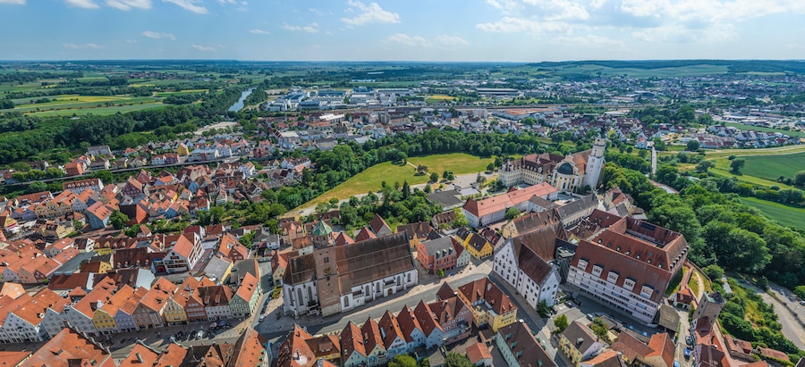 Une vue panoramique d’une ville historique, avec ses bâtiments aux toits rouges, une église imposante et les champs verdoyants qui l’entourent.