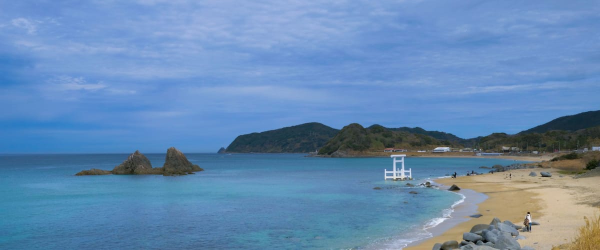 A beach with clear turquoise water, rocky outcrops, and a lifeguard tower.