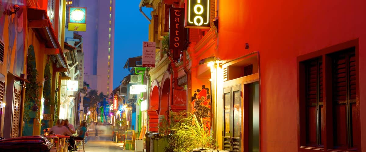 A brightly lit street with a tattoo parlor and a tall building with a 'village' sign.
