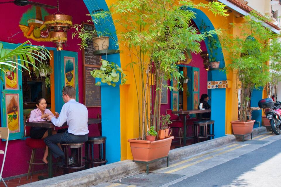 A colorful outdoor cafe with vibrant murals, potted plants, and a motorcycle parked nearby.