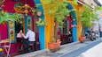 A colorful outdoor cafe with vibrant murals, potted plants, and a motorcycle parked nearby.