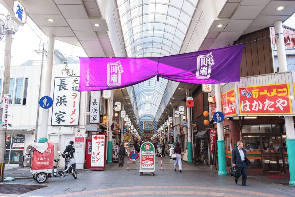A covered pedestrian walkway with shops, signs, and a bicycle.