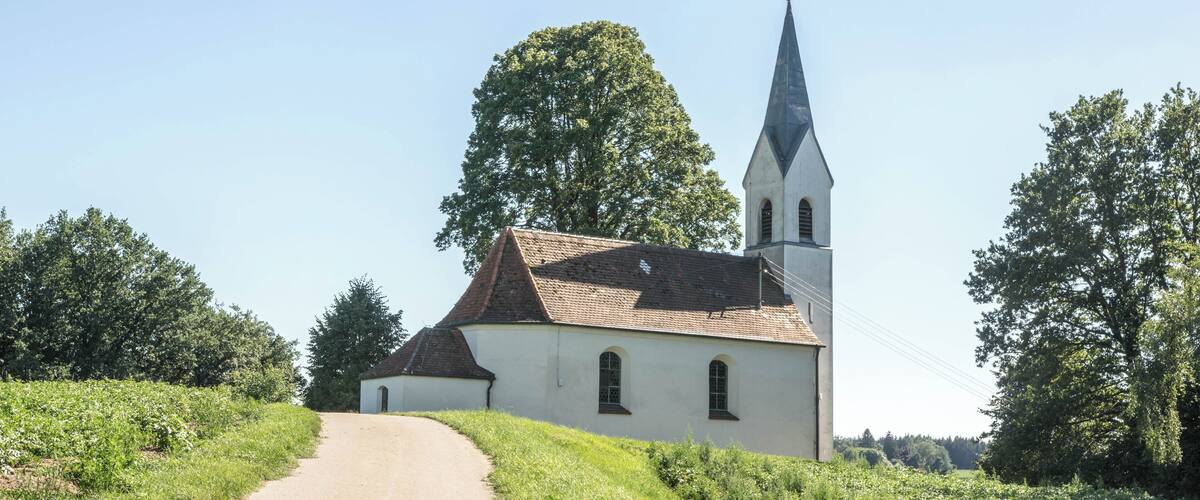A church with a tall steeple and a dirt road leading to it.