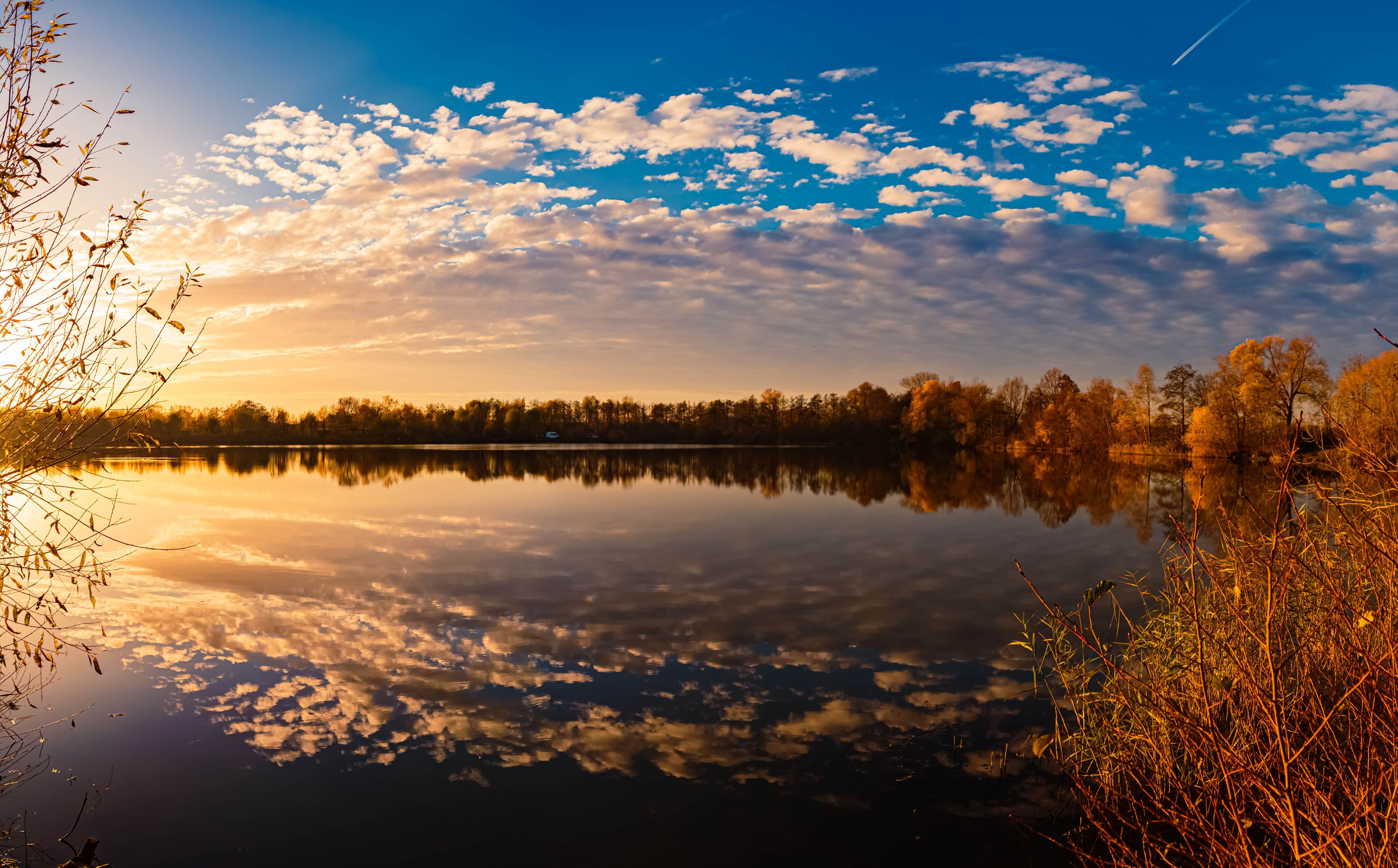 Ein ruhiger See spiegelt Himmel und Bäume wider.