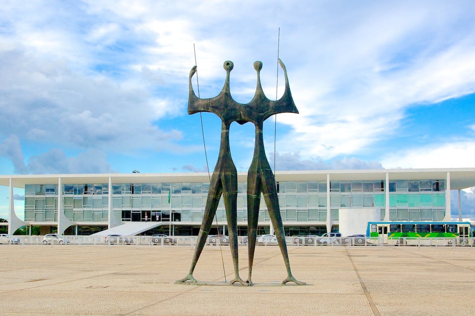 Um edifício moderno com fachada de vidro e uma escultura de figuras abstratas em frente.