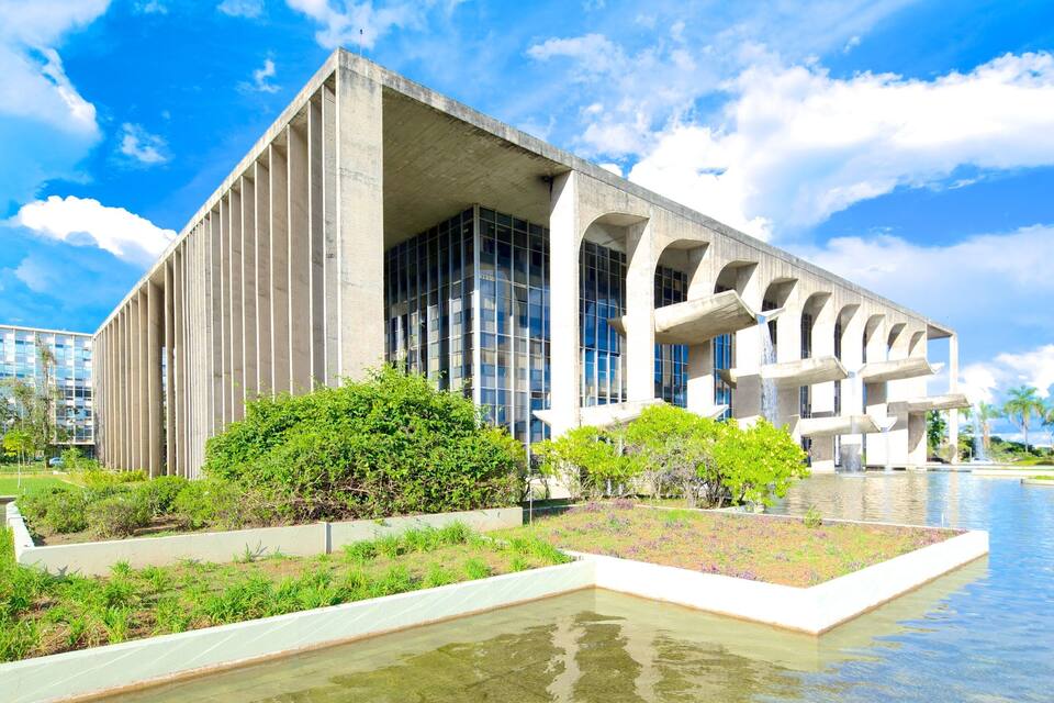 A modern building with a concrete facade and large windows, surrounded by a water feature and greenery.