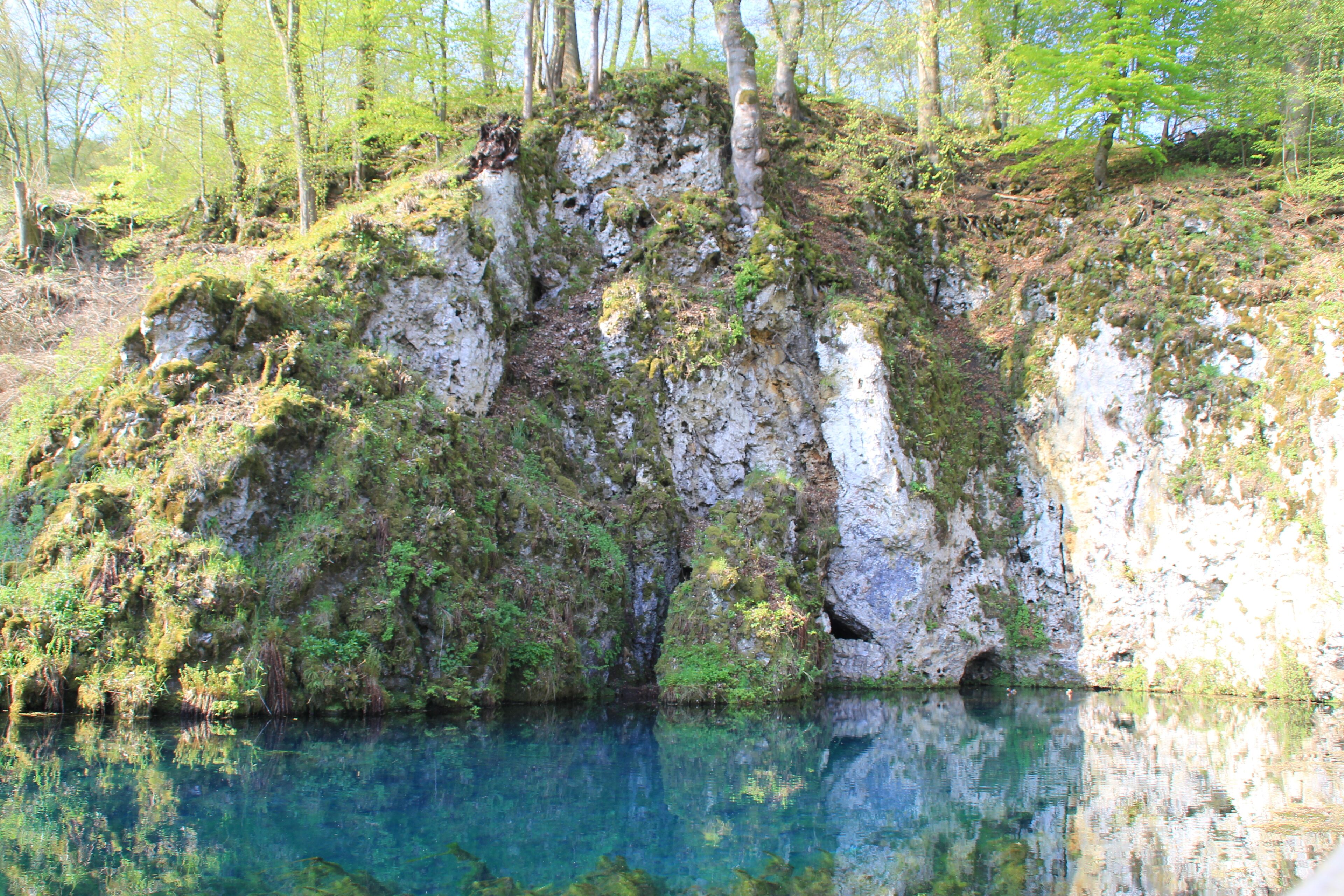 A clear lake surrounded by rocky cliffs with sparse vegetation.