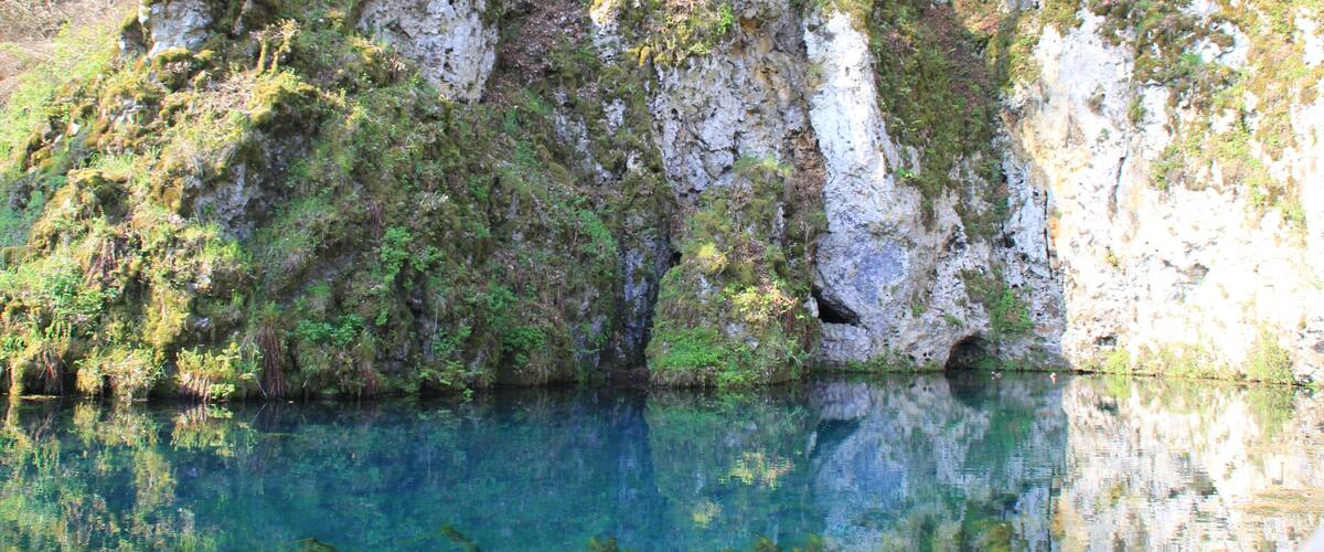 A clear lake surrounded by rocky cliffs with sparse vegetation.