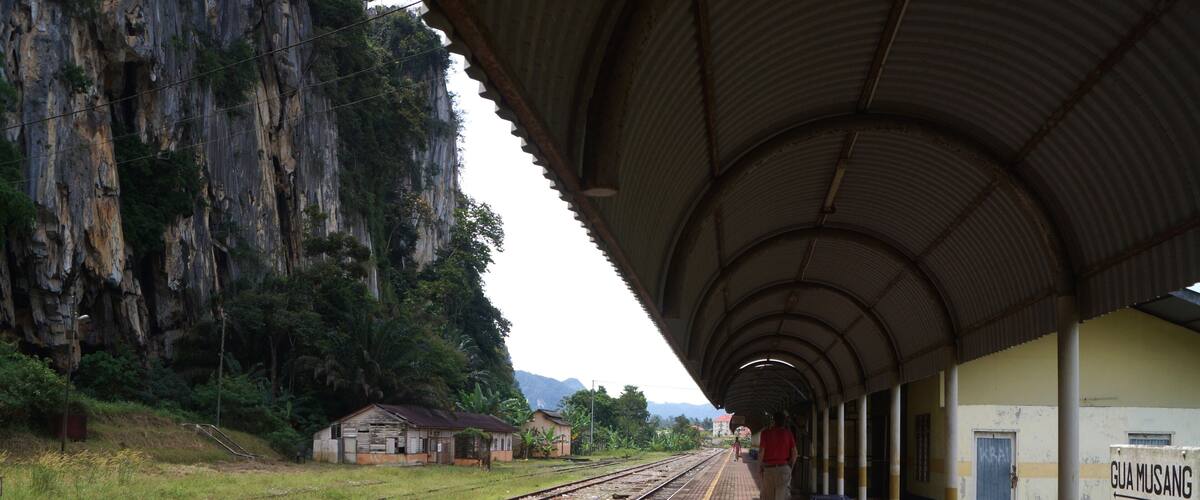 A railway station with tracks, a covered platform, and a sign that reads "GUA MUSANG".