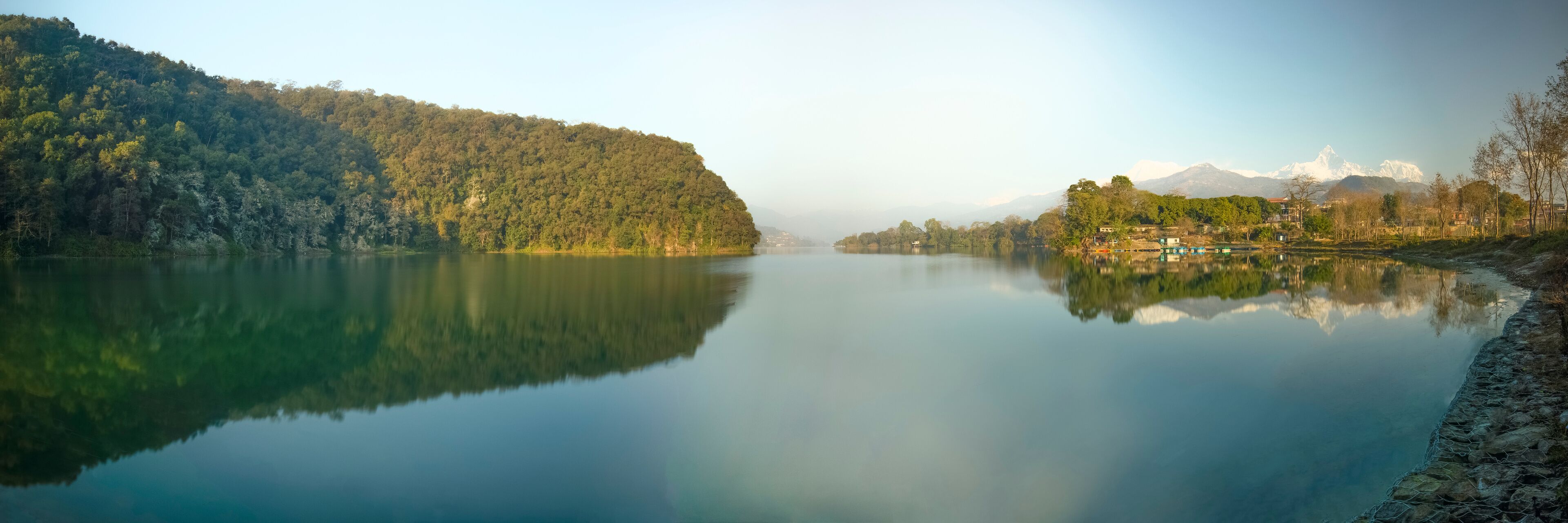A calm lake with a forested hillside on one side and a village with houses on the other.