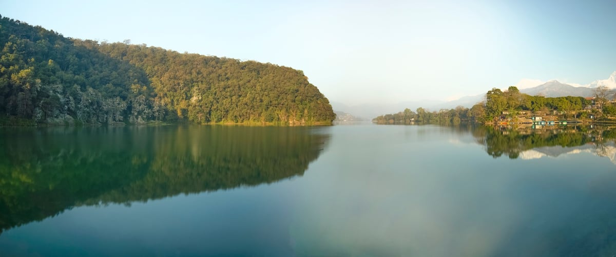 A calm lake with a forested hillside on one side and a village with houses on the other.