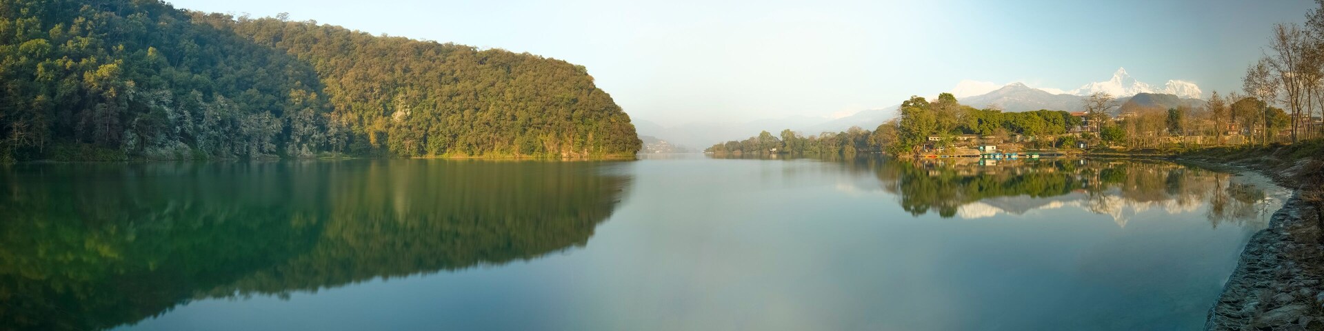 A calm lake with a forested hillside on one side and a village with houses on the other.