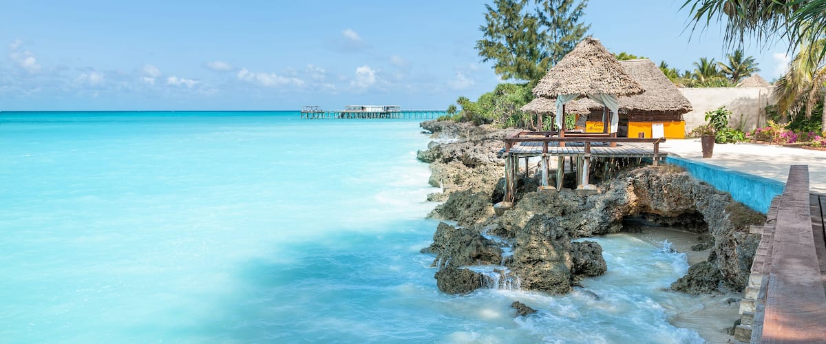 A tropical beach with clear turquoise waters, a thatched-roof hut, and a pier extending into the sea.