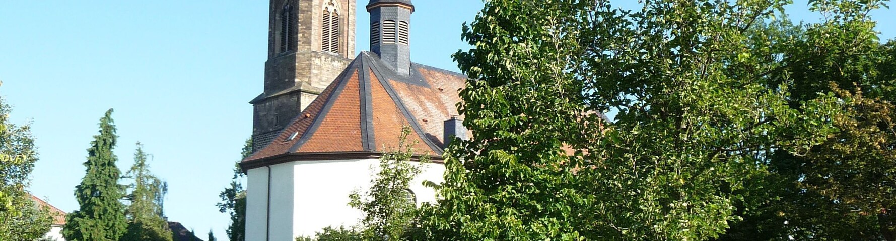 A church with a tall steeple and a clock tower, surrounded by greenery and yellow flowers.
