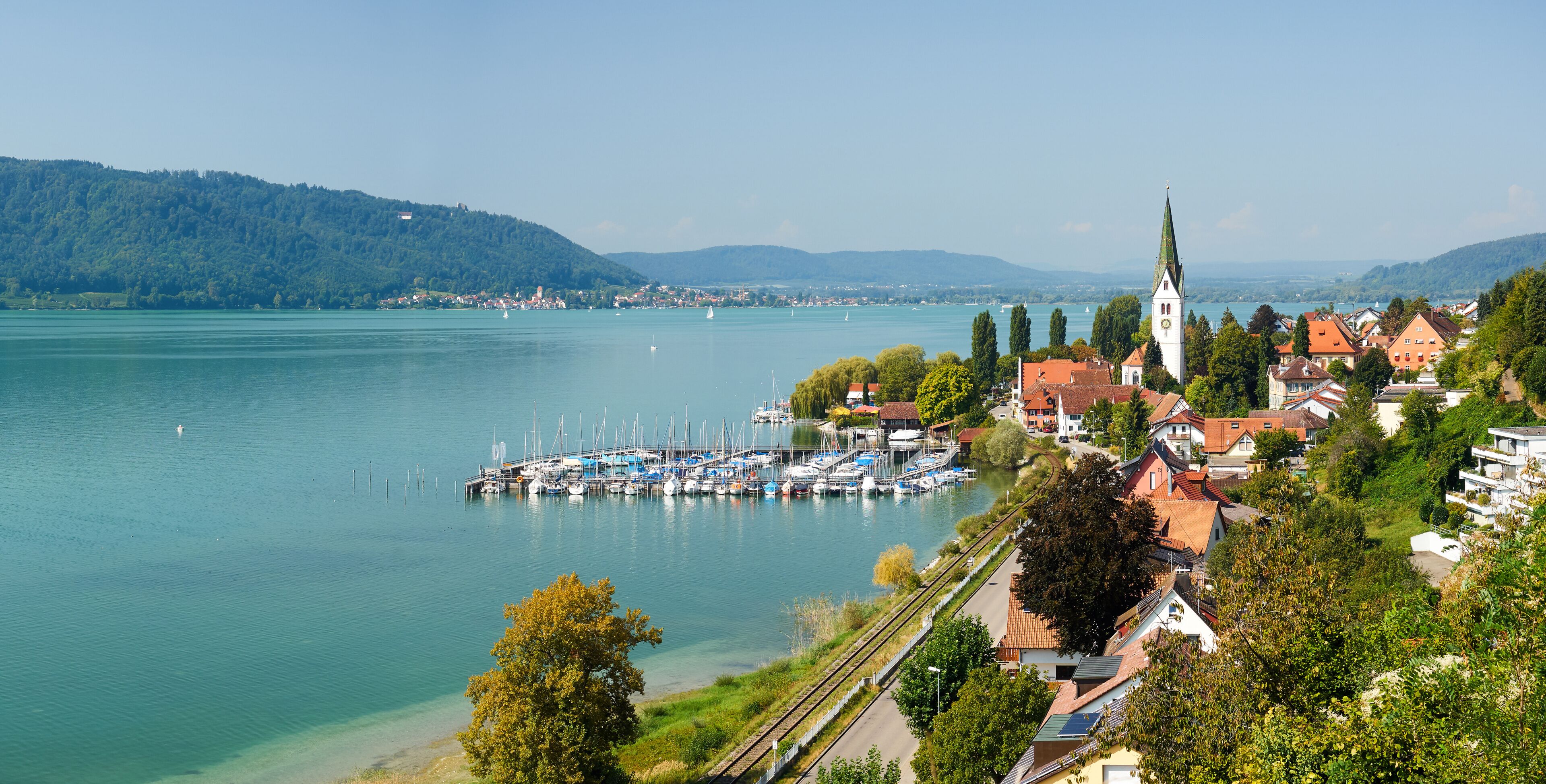 A lakeside town with a church, marina, and surrounding greenery.
