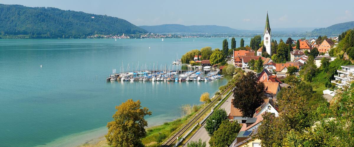A lakeside town with a church, marina, and surrounding greenery.