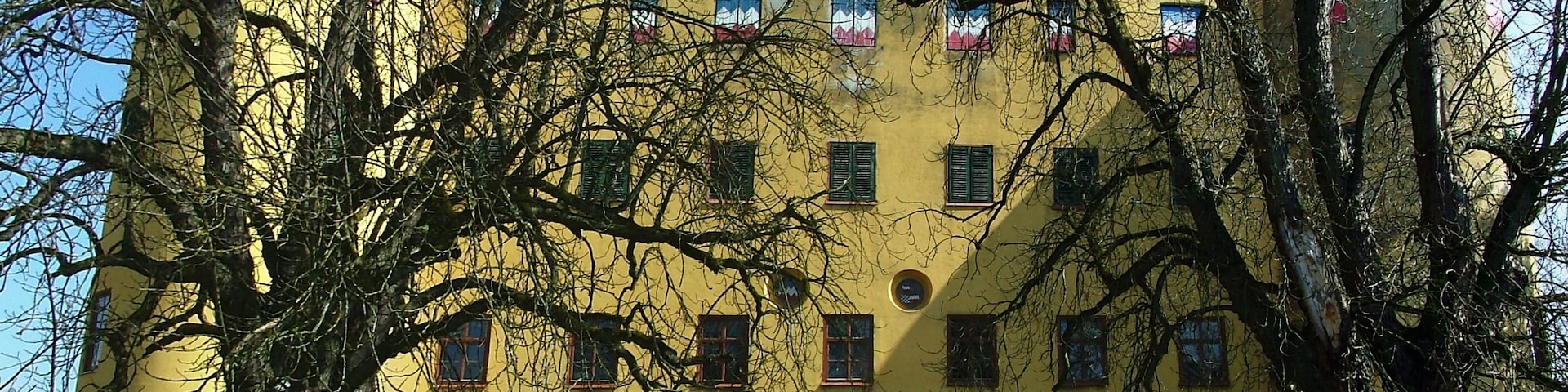 Un edificio amarillo con una gran entrada en arco, rodeado de árboles.