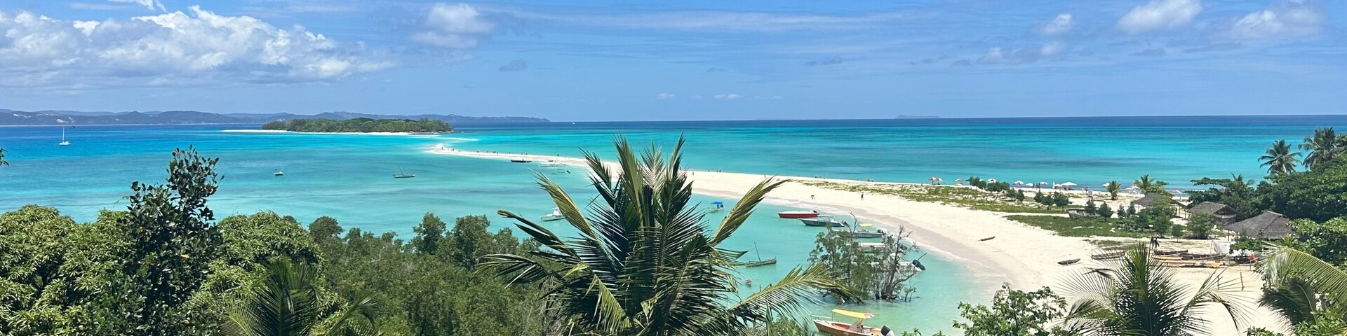 Uma praia tropical com águas turquesa cristalinas, palmeiras densas e uma ilha ao longe.