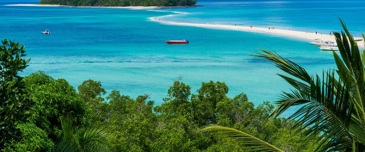 A tropical beach with clear turquoise waters, a small island, and a boat.