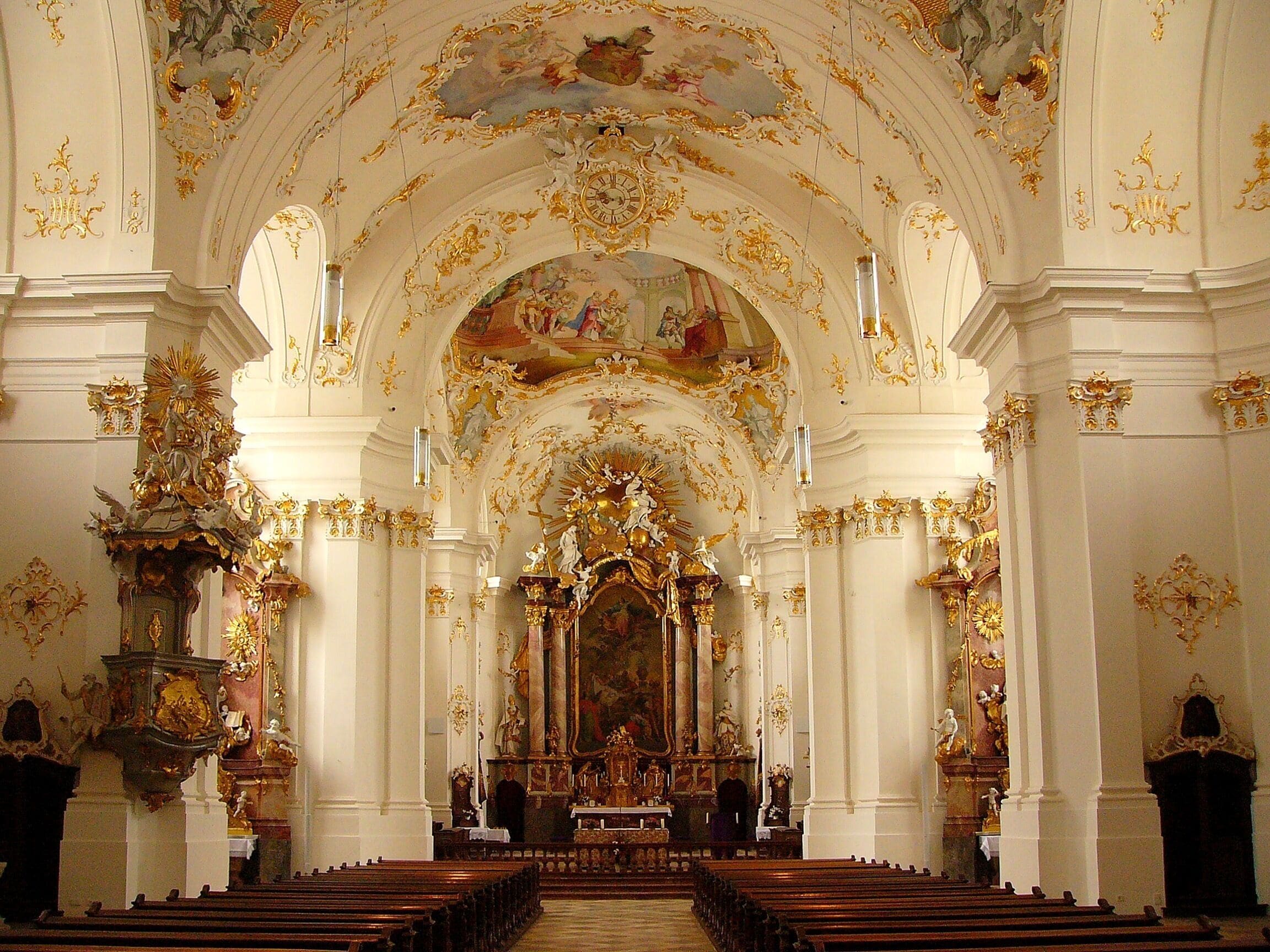 An ornate church interior with high ceilings, gold accents, and detailed frescoes.